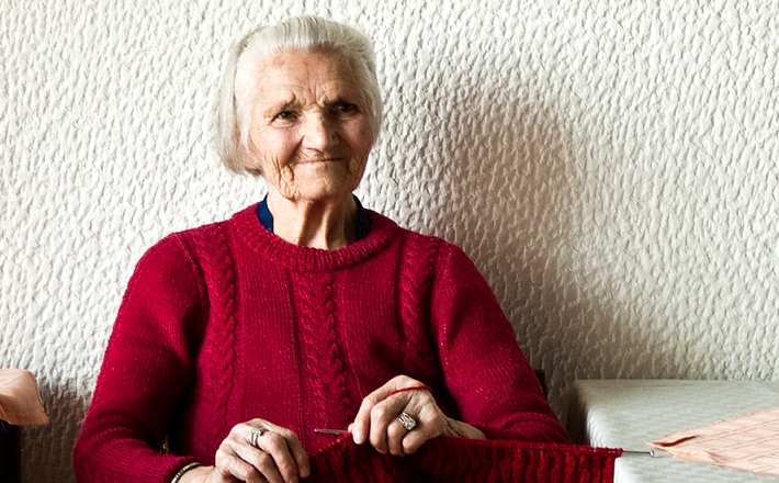 Old woman knitting red sweater