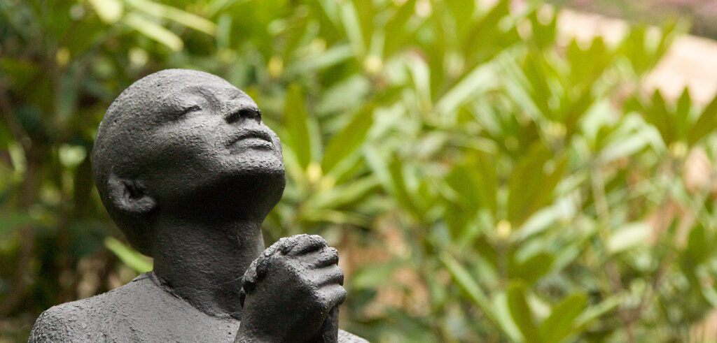 Statue of woman praying in garden setting