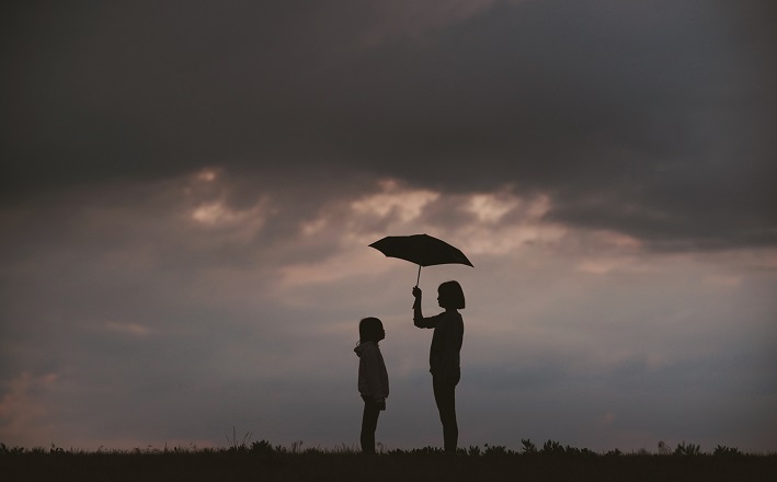 Woman holding umbrella over child against stormy backdrop