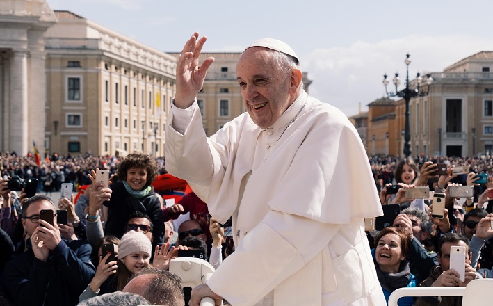 Pope Francis waves to crowd outdoors.