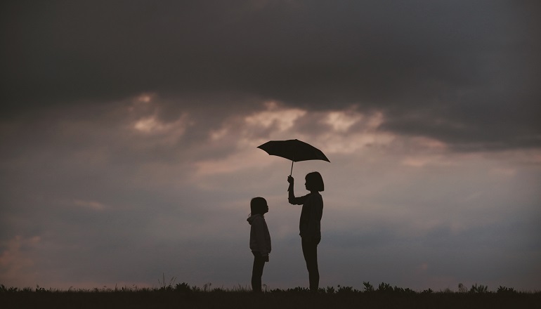 Woman holding umbrella over young person's head in storm