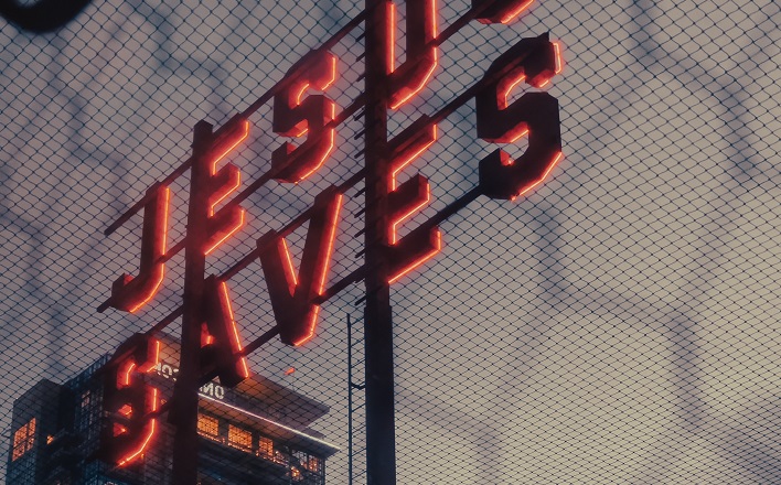 Jesus Saves neon sign behind chicken wire