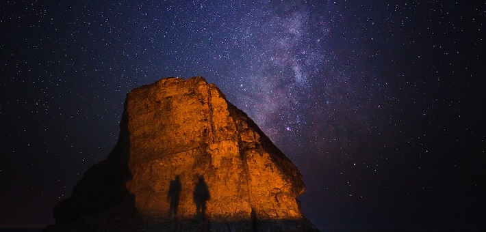 Night sky with stars, silhouetted figures visible in foreground.