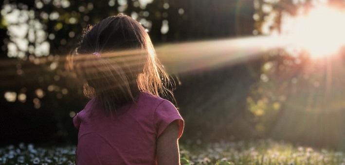 Girl in field of flowers gazing at sunset