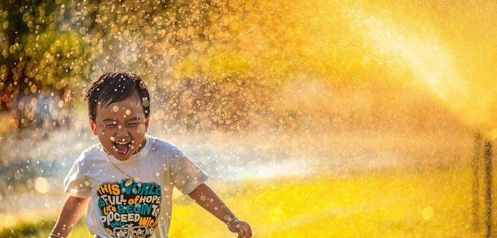 Boy under sprinkler in summer grass