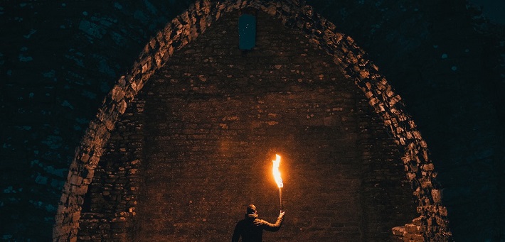 Figure holding torch under large stone arch