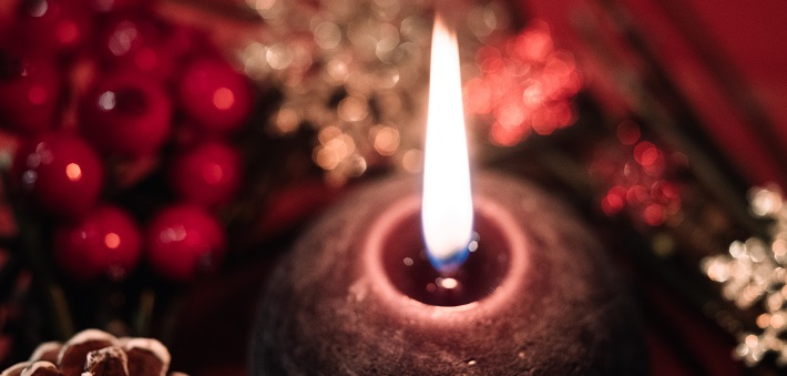 candle burning with Christmas decorations in background