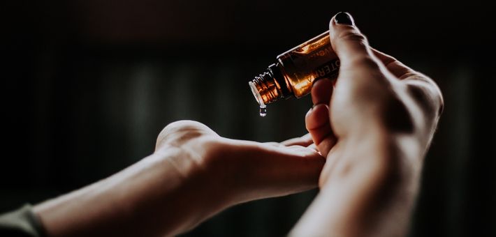 person holding a glass amber bottle dripping oil into her hand