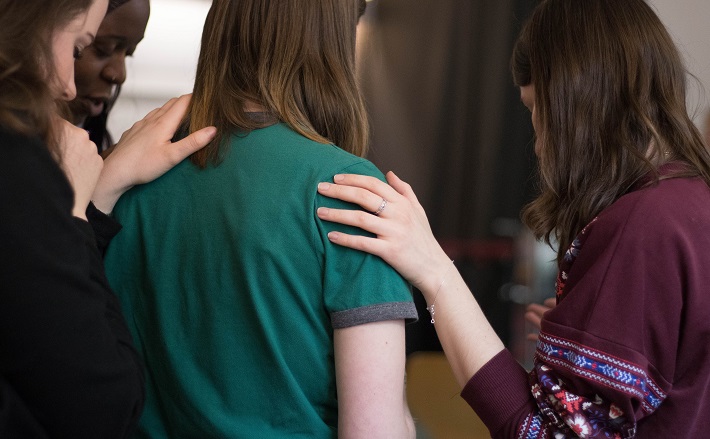 Women laying hands on woman wearing green shirt.