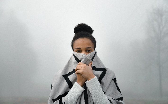 Woman in foggy landscape clutching sweater over mouth