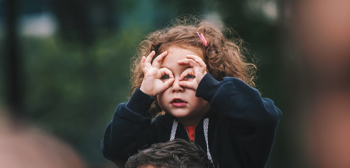 Girl on someone's shoulders uses fingers as play binoculars