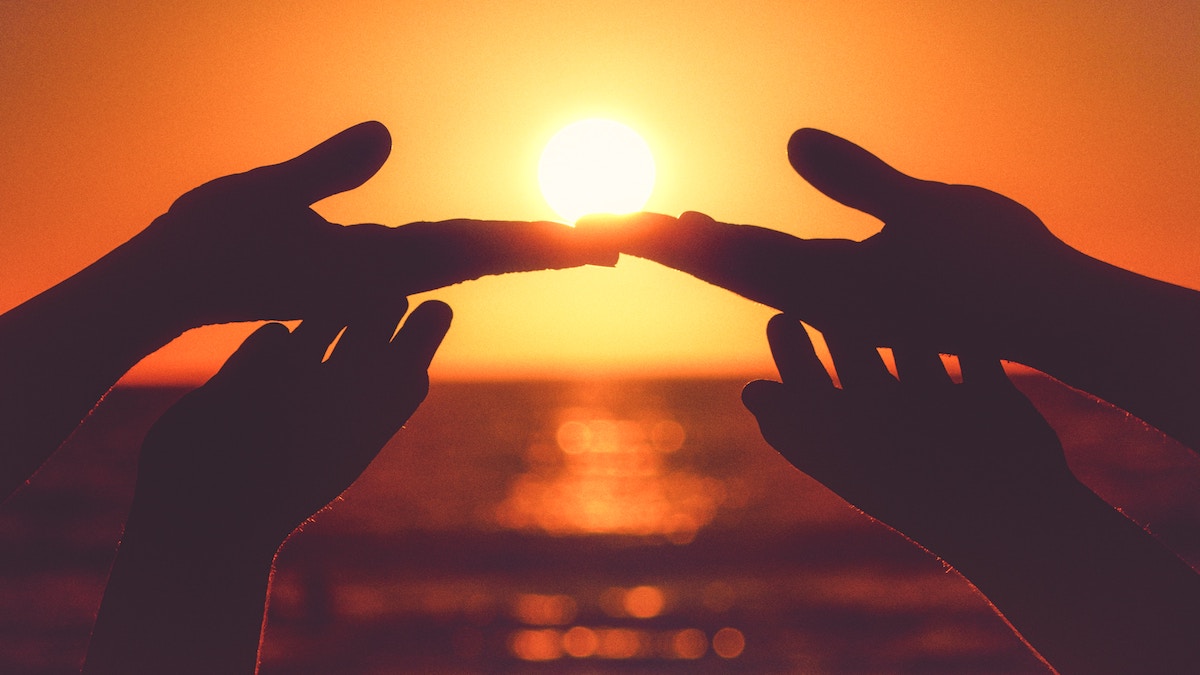 Hands touching in front of setting sun