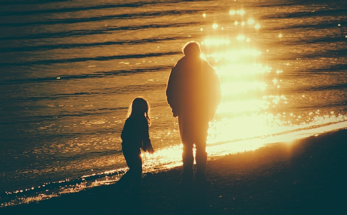 Two silhouetted figures at lakeshore in golden hour