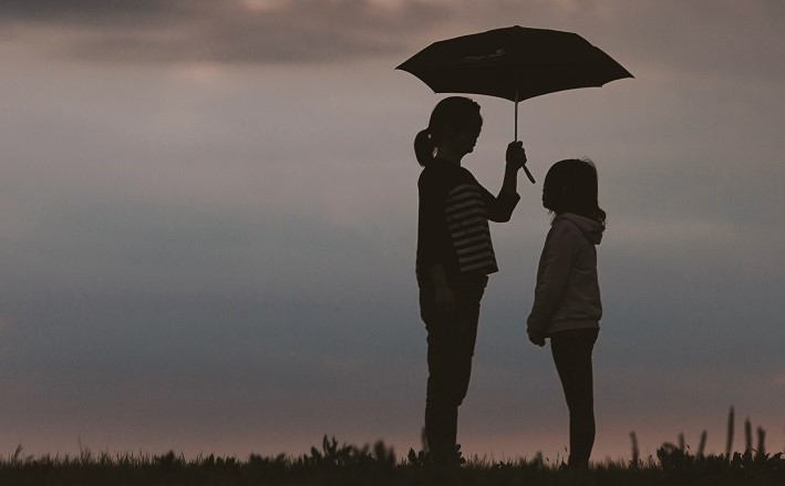 Woman holding umbrella over young person