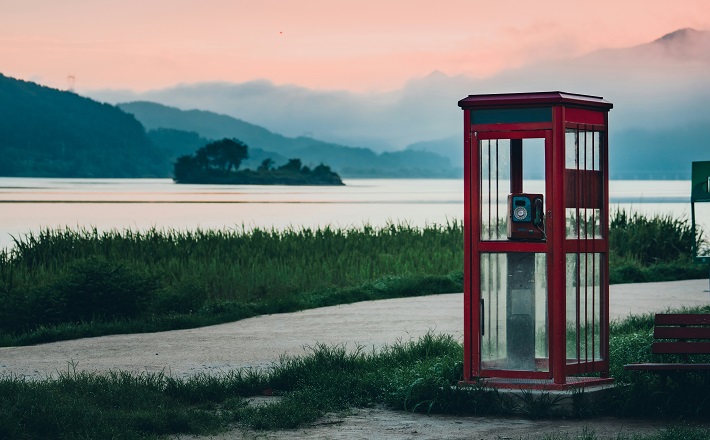 Red phone booth next to body of water at sunrise