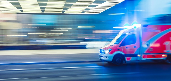 Ambulance with flashing lights streaming past lit building