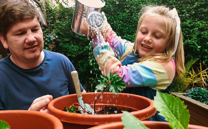 Girl watering potted plants outside while man helps