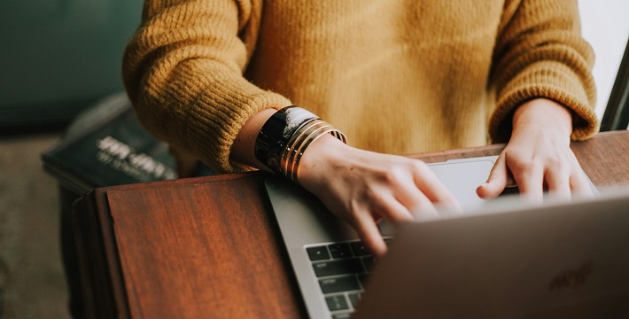 Person with mustard sweater typing into laptop