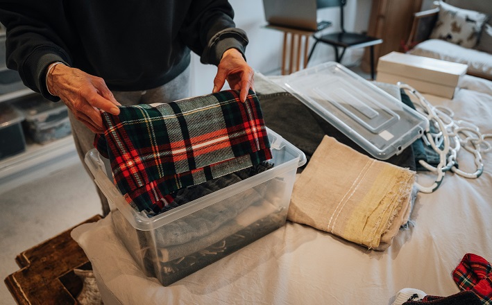 Decluttering a household, putting blankets in clear bin.