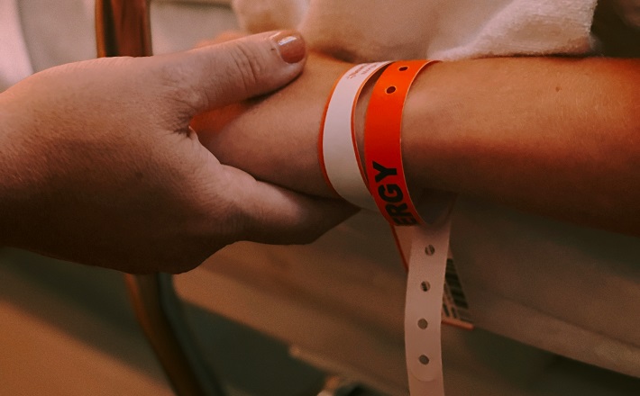 Caregiver holding the hand of patient with red ID wristbands