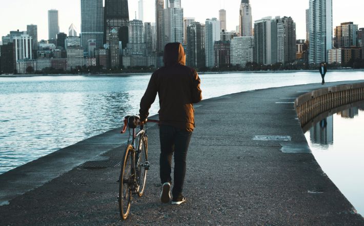 Person walking bike in front of cityscape in cold weather