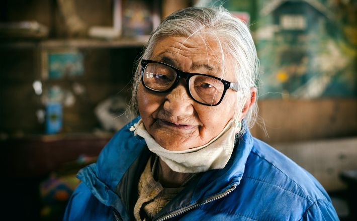 Woman with mask and thick glasses gazing steadily forward at camera