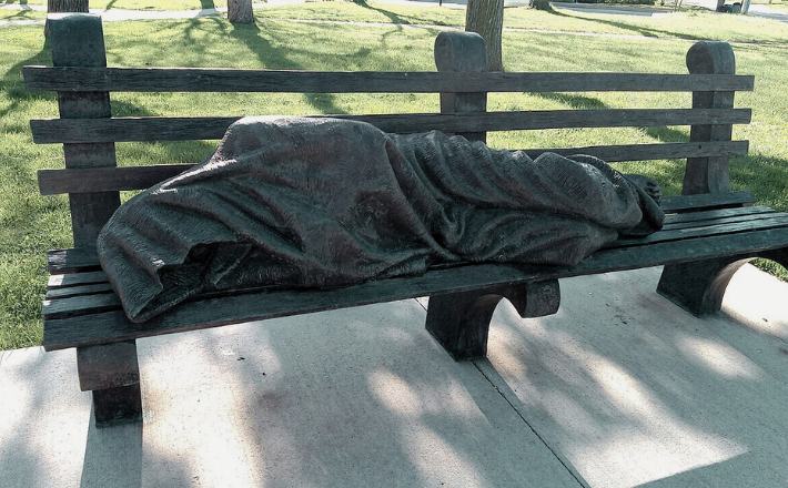 Photo of a bronze sculpture by Canadian sculptor Timothy Schmalz, on a bench beside St. Clement's church in Cambridge, Ontario.