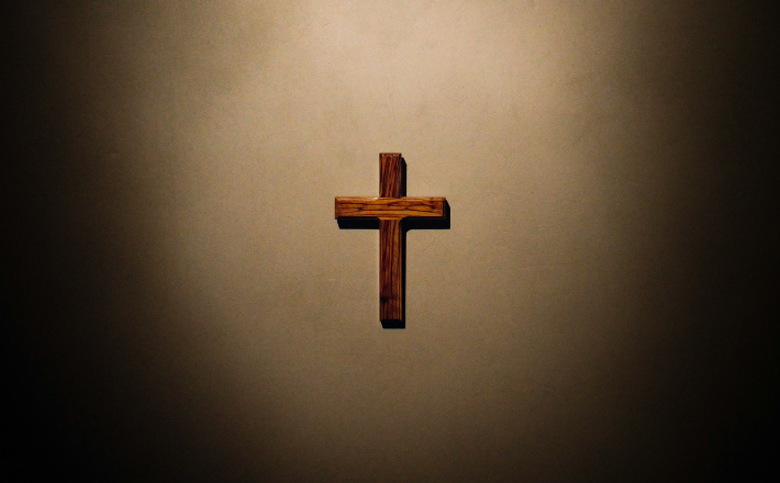 photo of a starkly lit wooden cross on a beige wall