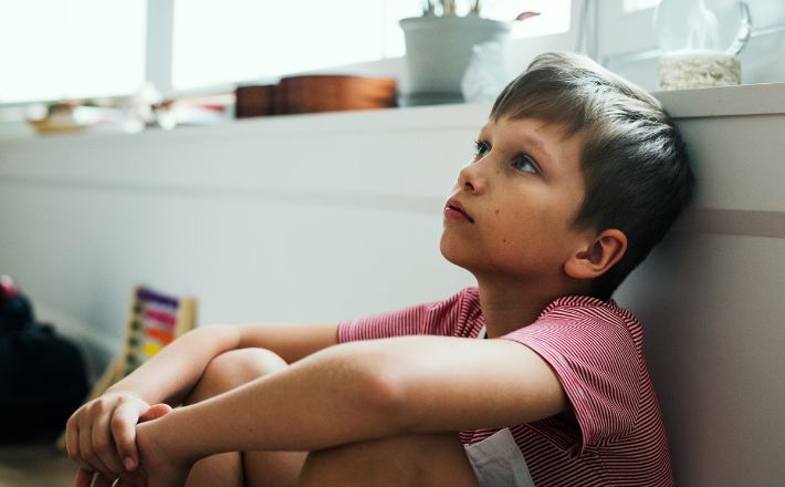 Boy looking up to the left while leaning against a white backdrop