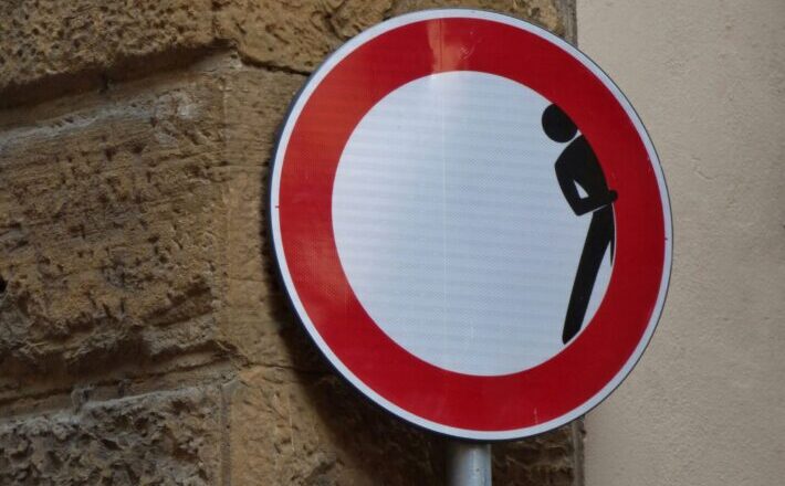 Street sign with figure peeking from behind a wall