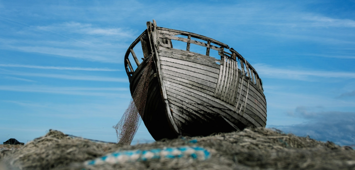 photo of an old gray wooden boat with fishing net beneath it