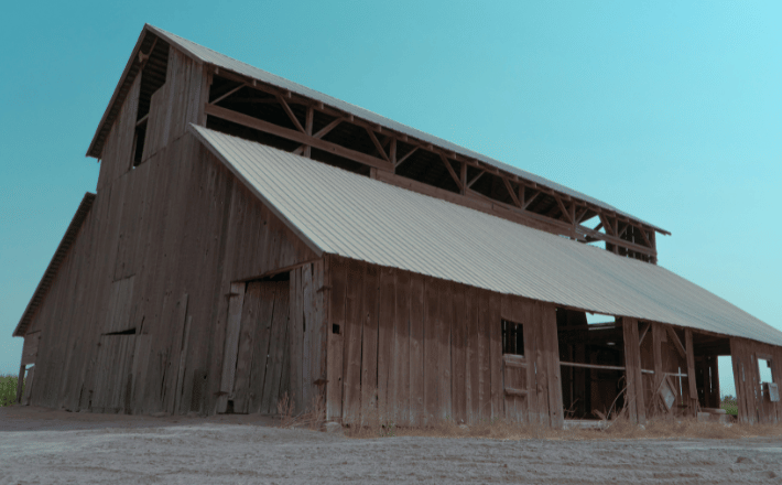 an old barn sits in the middle of a field