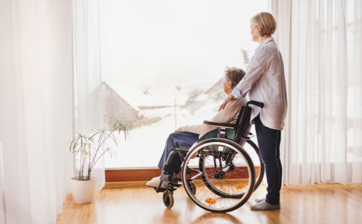 Woman and her mother look out window together.