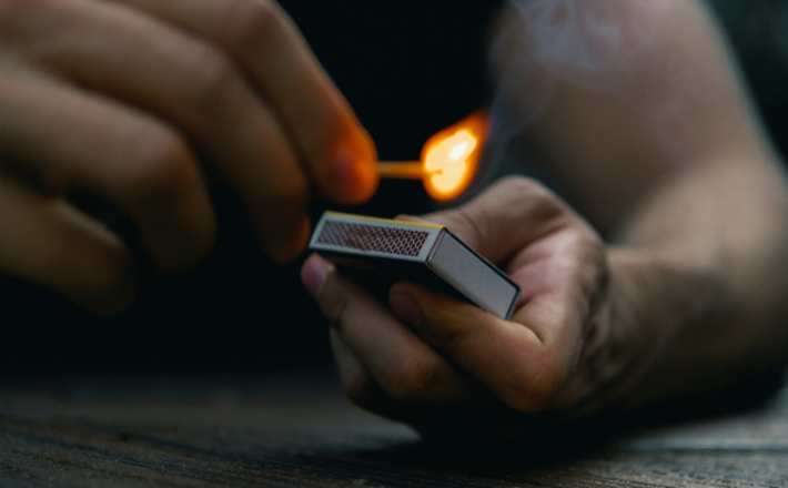 Person holding black and white match box with a lit match