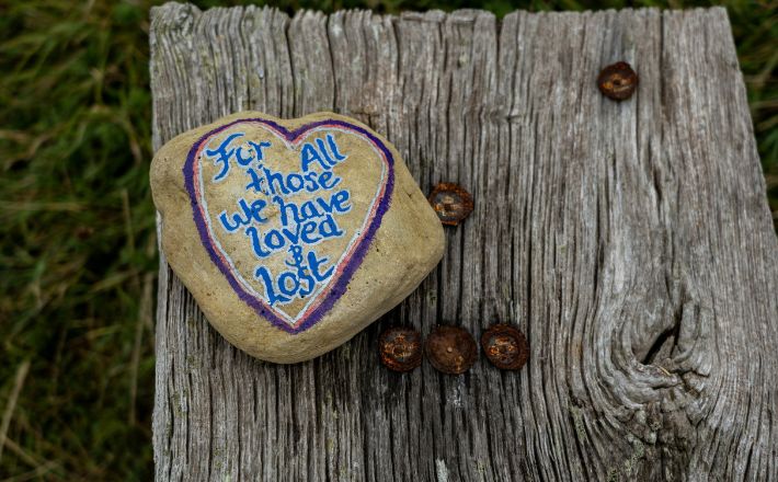 Rock on wood background with message: For all those we have loved and lost