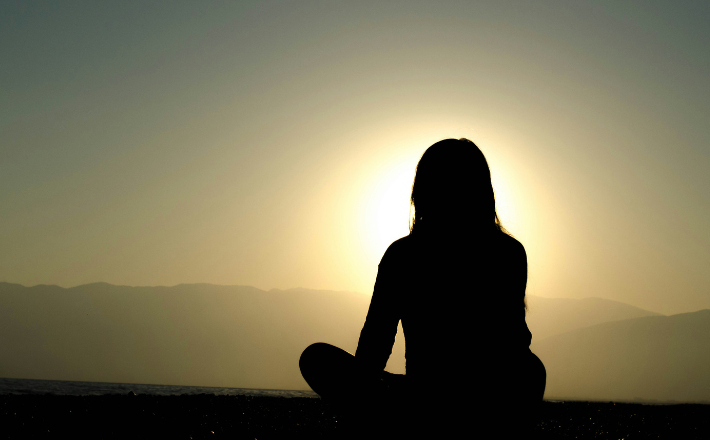 Silhouette of the back of a woman sitting on sand during a sunset