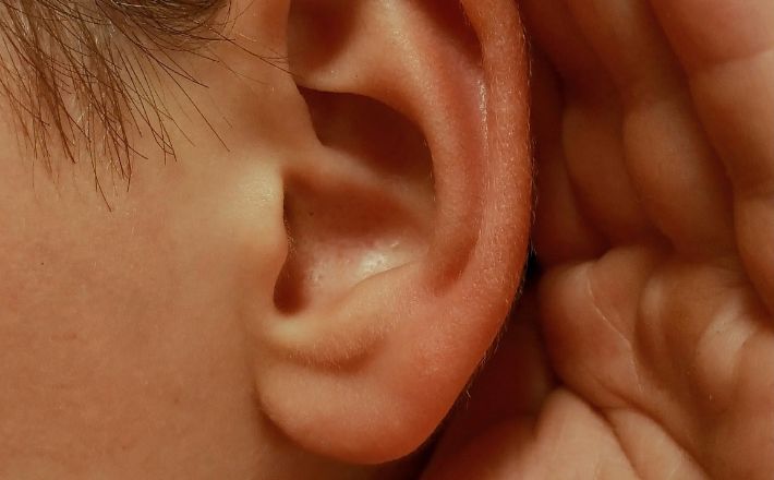 Closeup of ear with hand cupped behind to signify close listening