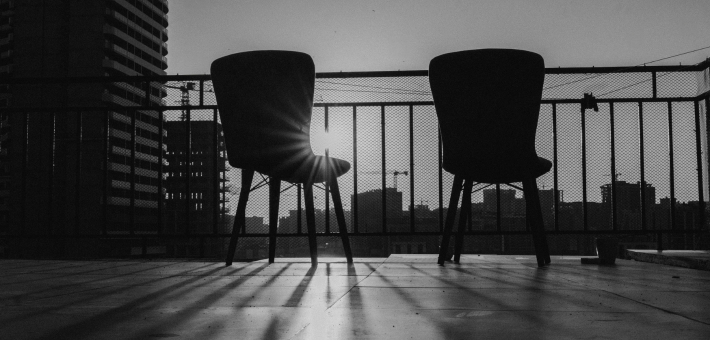 black and white photo of two chairs with sun rising between