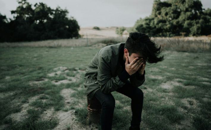 Young man holding face in hands while kneeling on grass